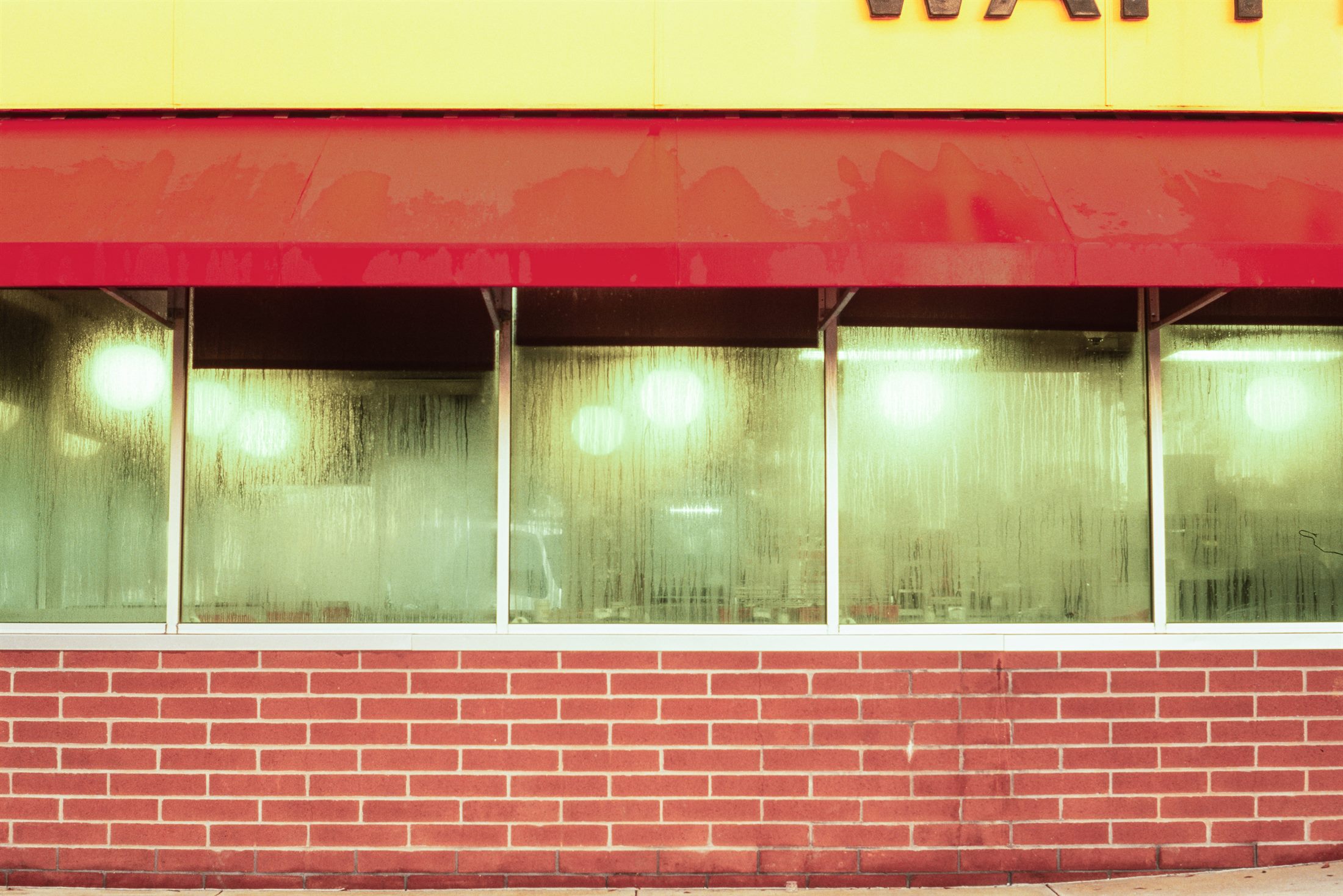 A storefront with a yellow sign and red awning above steamed, water-streaked windows and a brick base.